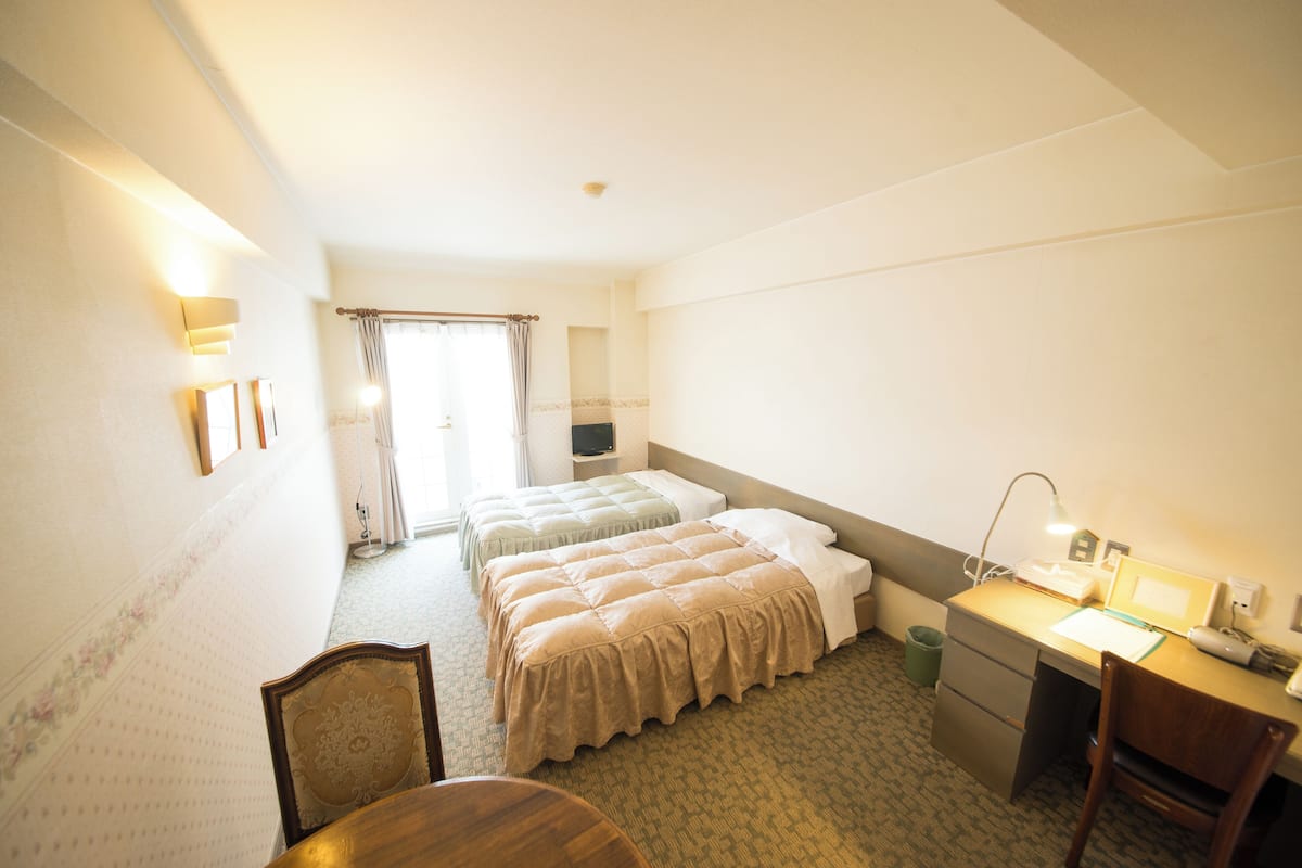 A hotel room with two beds, a desk, a chair, a lamp, and a trash bin.