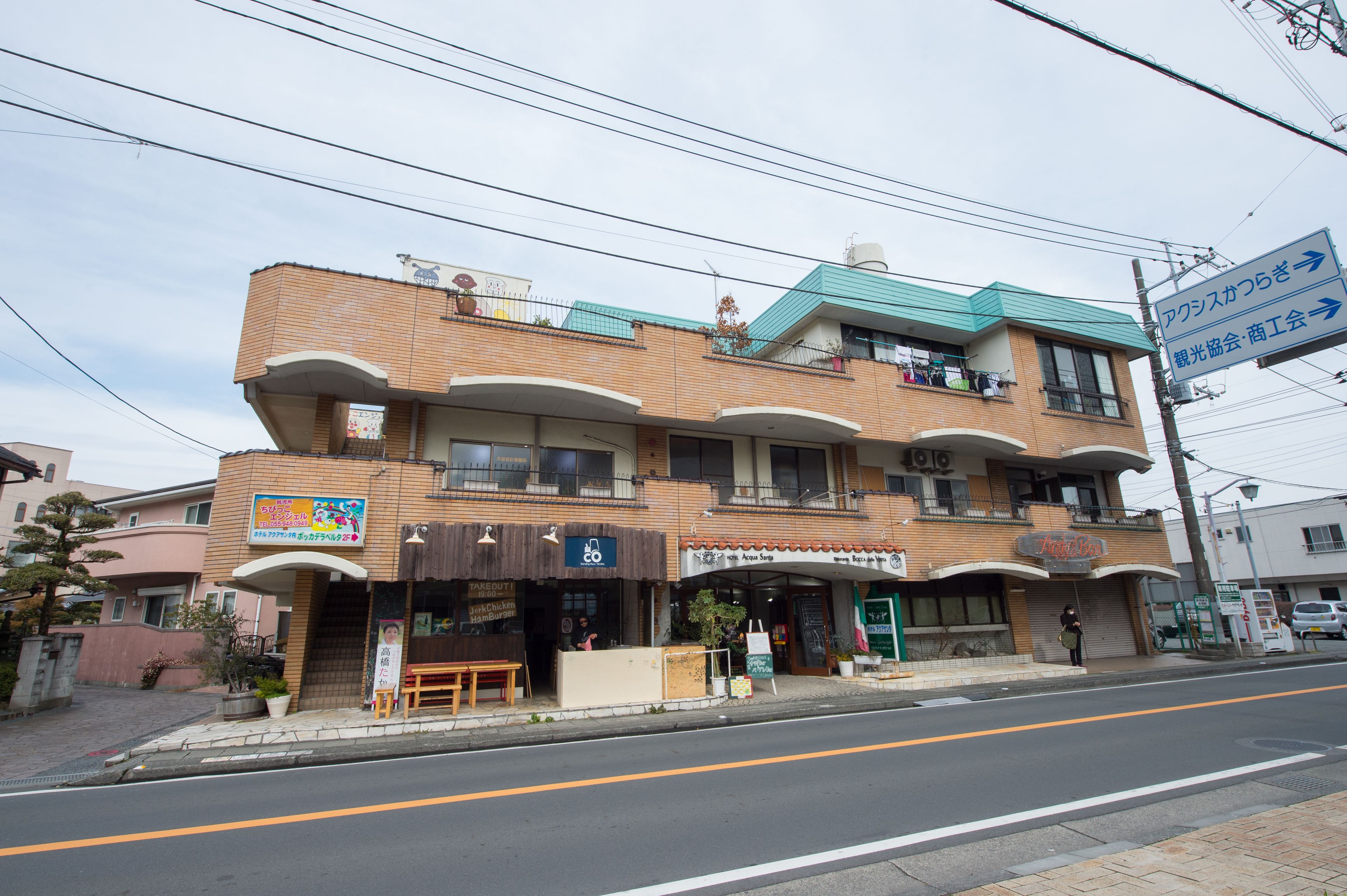 Un edificio de varios pisos con diferentes tiendas en la planta baja, incluyendo un restaurante y una tienda de conveniencia.