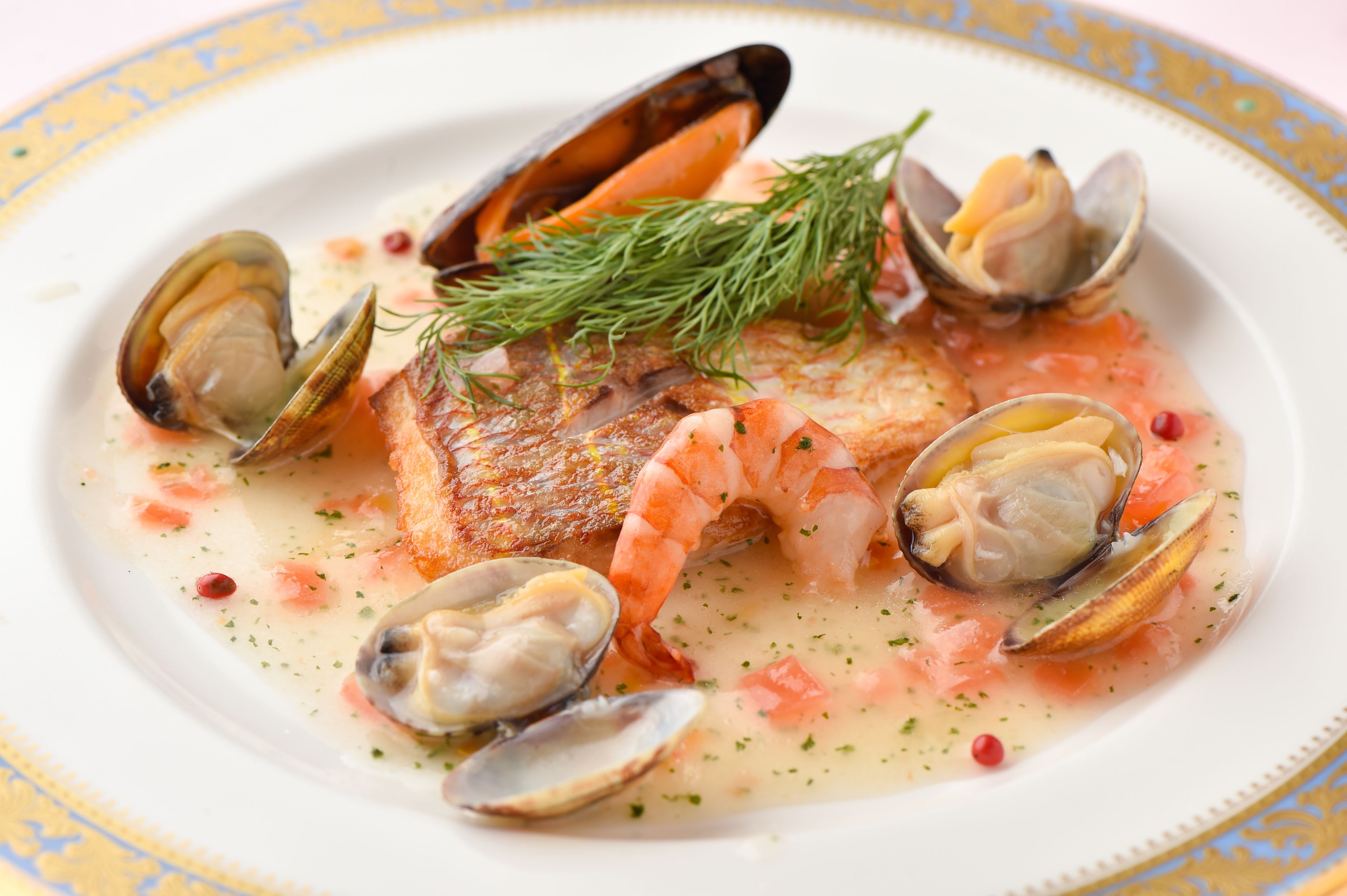 Un plato de mariscos con almejas, camarones y un trozo de pescado, adornado con eneldo.