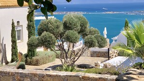 Muro de piedra con una hamaca y un árbol en primer plano, con vistas a la costa y un cielo despejado.