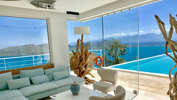 Una sala de estar moderna con sofá, mesa de centro y sillones, ventanas amplias con vistas a una piscina y montañas.
