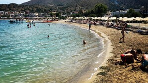 Una playa con agua cristalina, gente nadando y tomando el sol, y montañas al fondo.