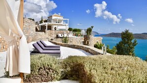 Una villa costera con fachada de piedra, asientos al aire libre y vistas al mar.