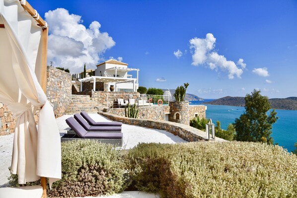 A coastal villa with a stone facade, outdoor seating, and a view of the sea.