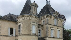 Une table dressée à l’extérieur, recouverte d’une nappe rouge, entourée de chaises en métal, devant un bâtiment historique surmonté d’une toiture à tourelles.