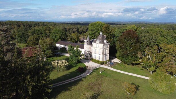 Un grand bâtiment historique, doté d’une tour imposante, entouré d’une végétation luxuriante et d’une pelouse bien entretenue.