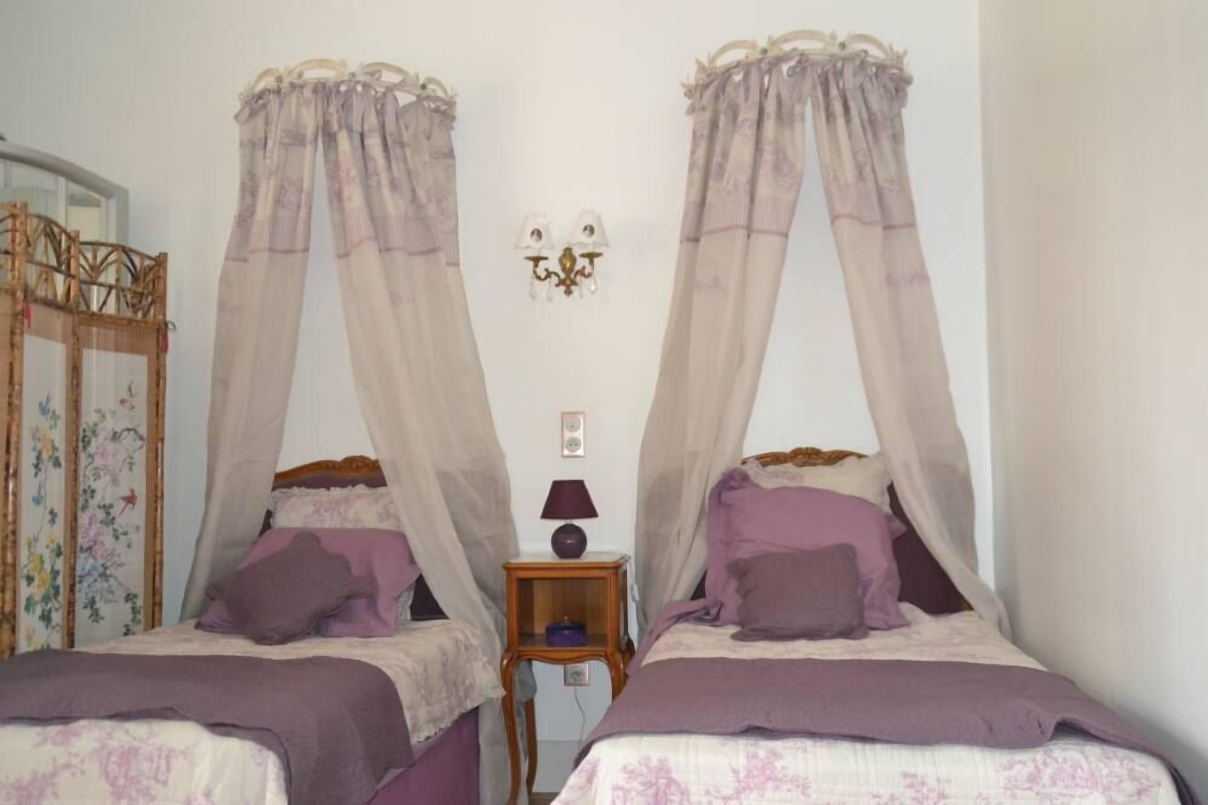 Un dormitorio con dos camas, cada una con dosel. Hay una mesita de noche con lámpara entre las camas.