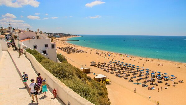 A beach with a long promenade, umbrellas, and people.
