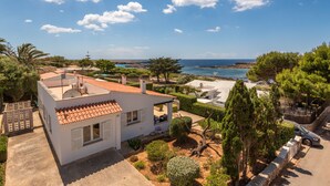 Una villa costera con techo de tejas, rodeada de vegetación y vista al mar.