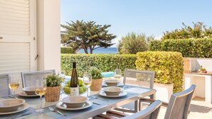 Un área de comedor al aire libre con una mesa preparada para cuatro personas, una botella de vino y vista al mar.