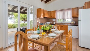 Una cocina moderna con armarios de madera, una mesa de comedor preparada para cuatro comensales y un amplio ventanal con vistas a la vegetación.