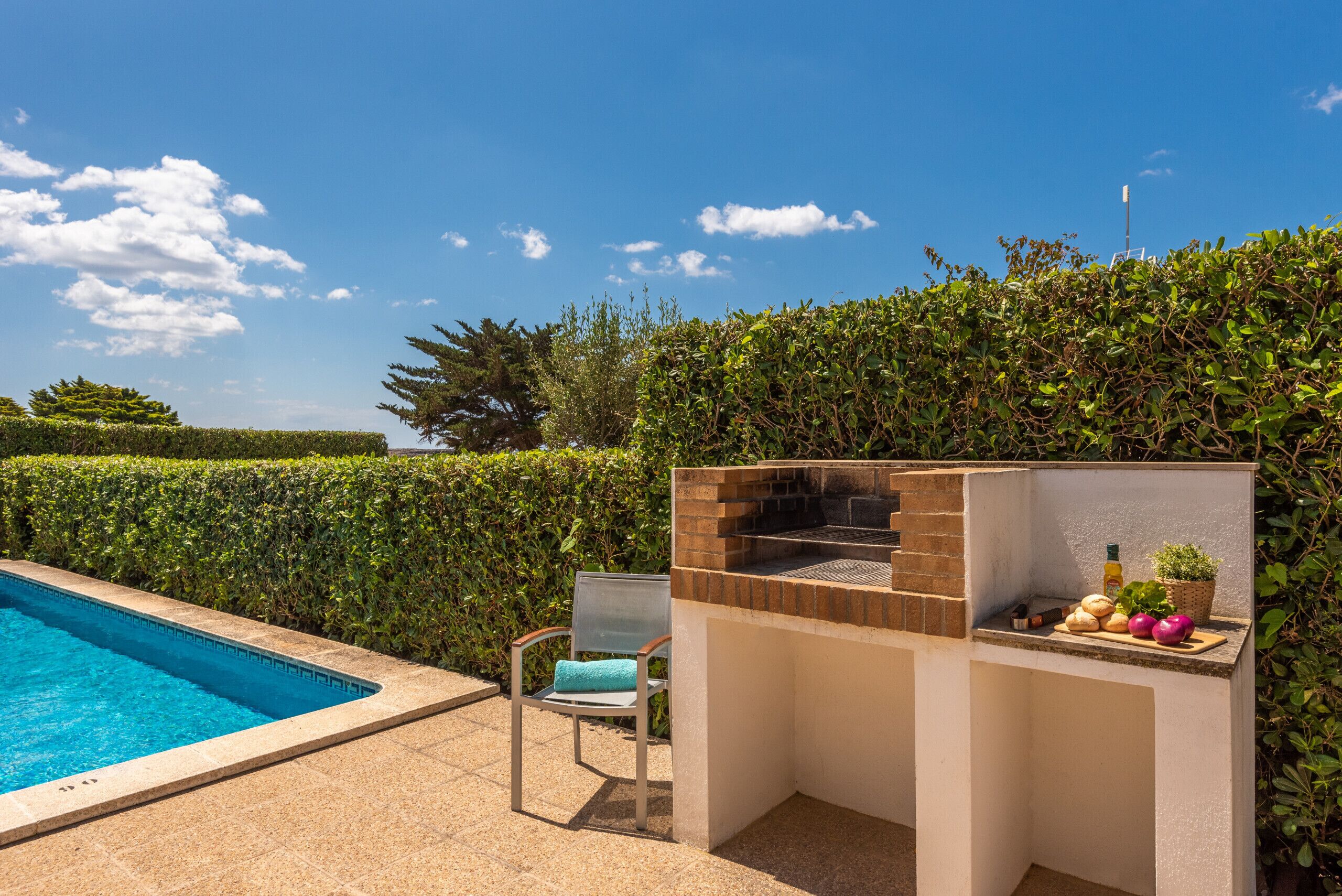 Zona junto a la piscina con una parrilla y una silla.