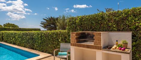 Zona junto a la piscina con una parrilla y una silla.