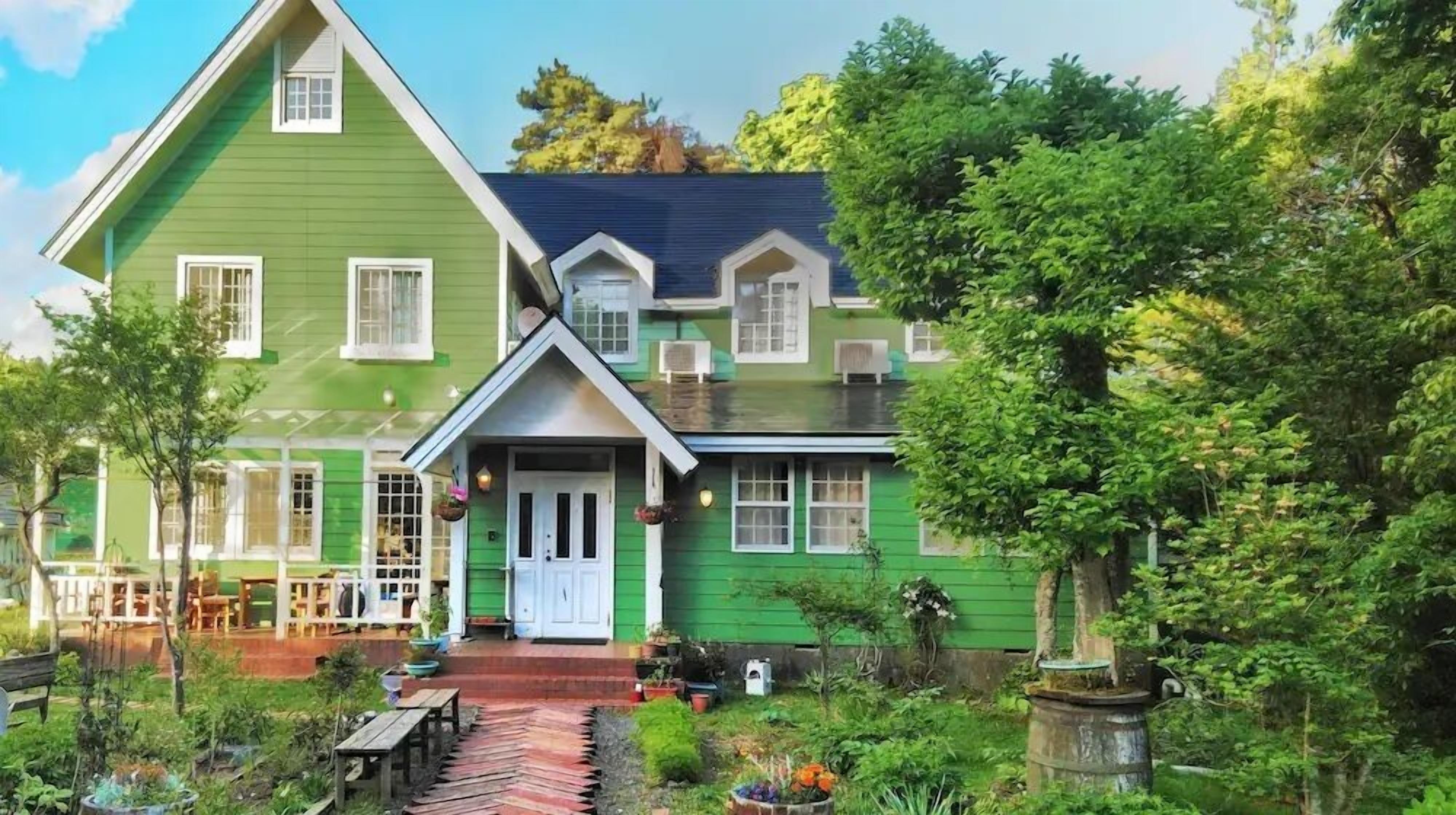 A green house with a porch, a small garden, and a wooden bench.