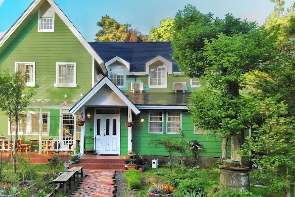 A green house with a porch, a small garden, and a wooden bench.