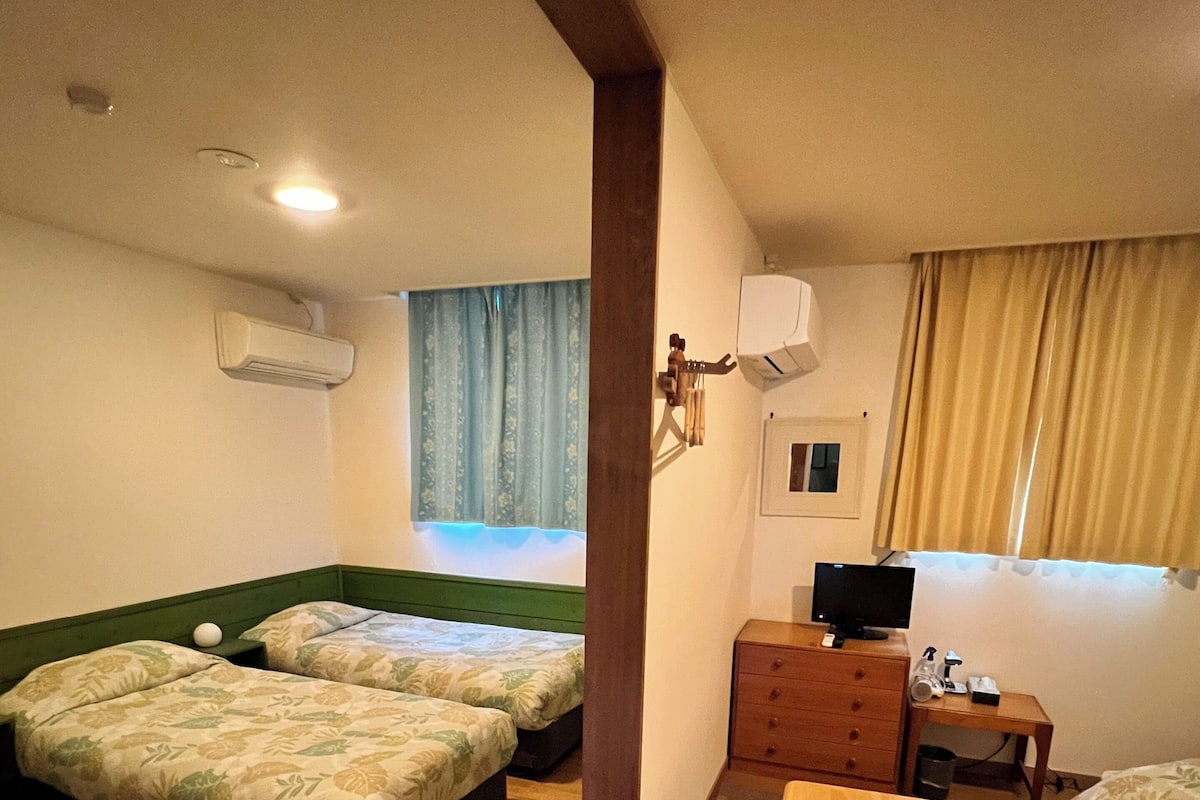 A hotel room with two beds, a wooden dresser, a television, and a window with curtains.
