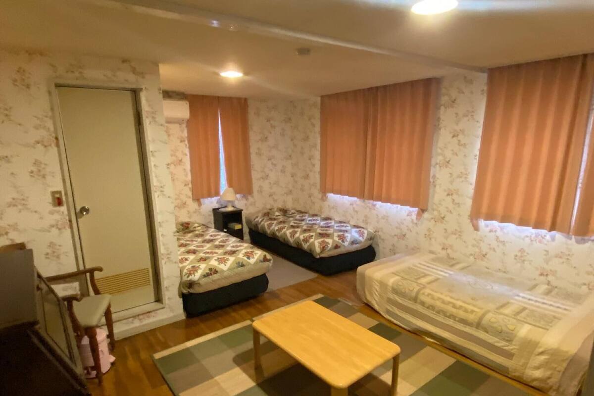 A small, cozy room with two single beds, a wooden bench, a small table, and a door.