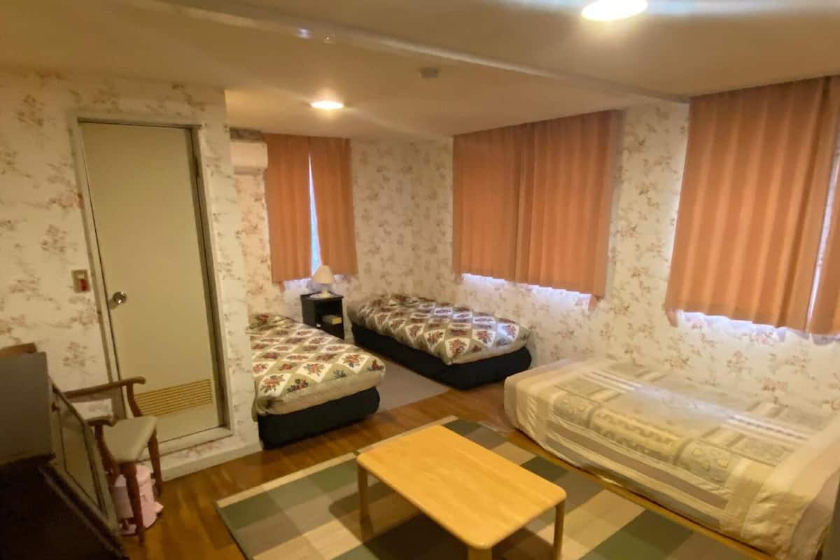 Una habitación pequeña y acogedora con dos camas individuales, un banco de madera, una mesita y una puerta.