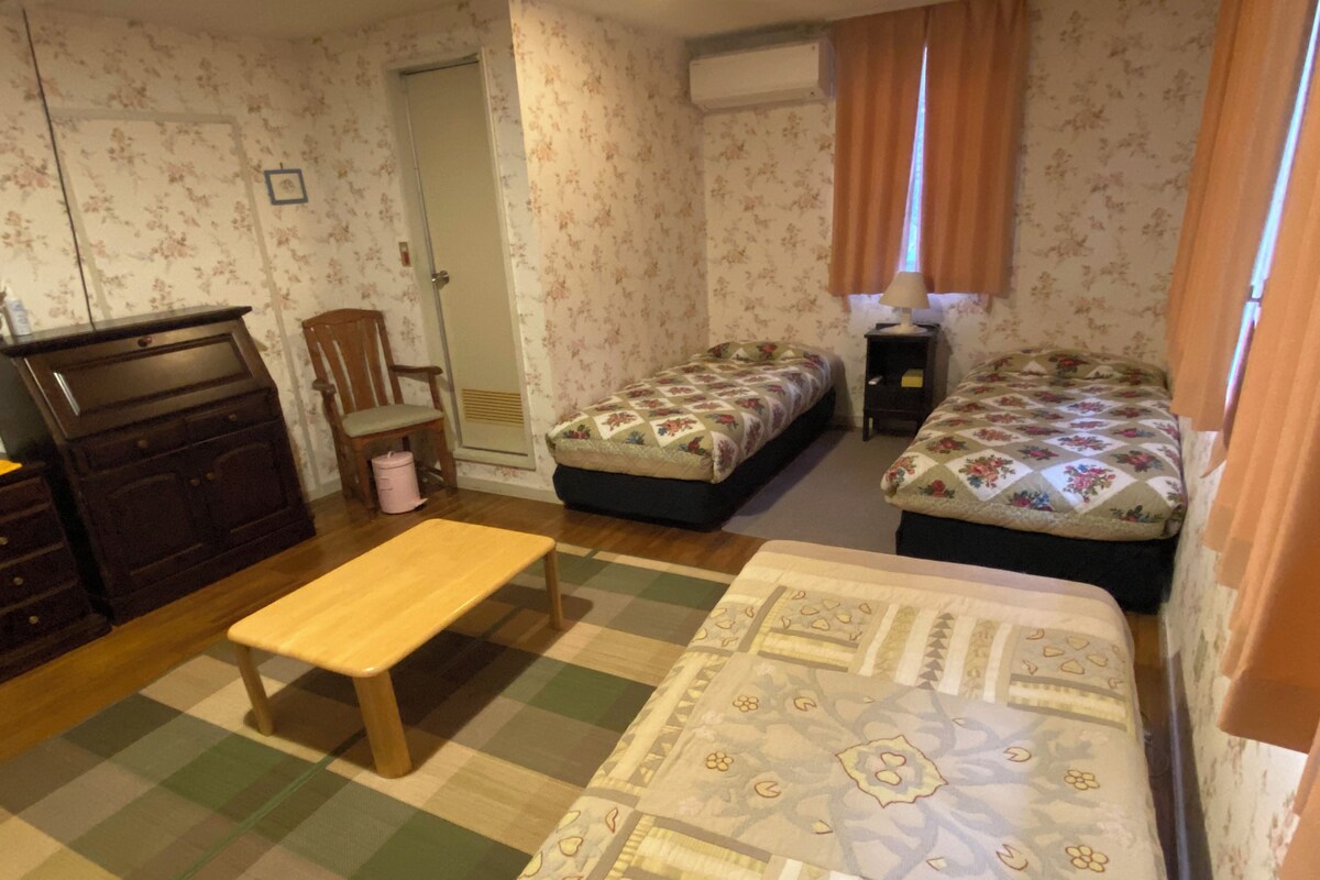 A bedroom with two beds, a wooden bench, a dresser, and a chair.