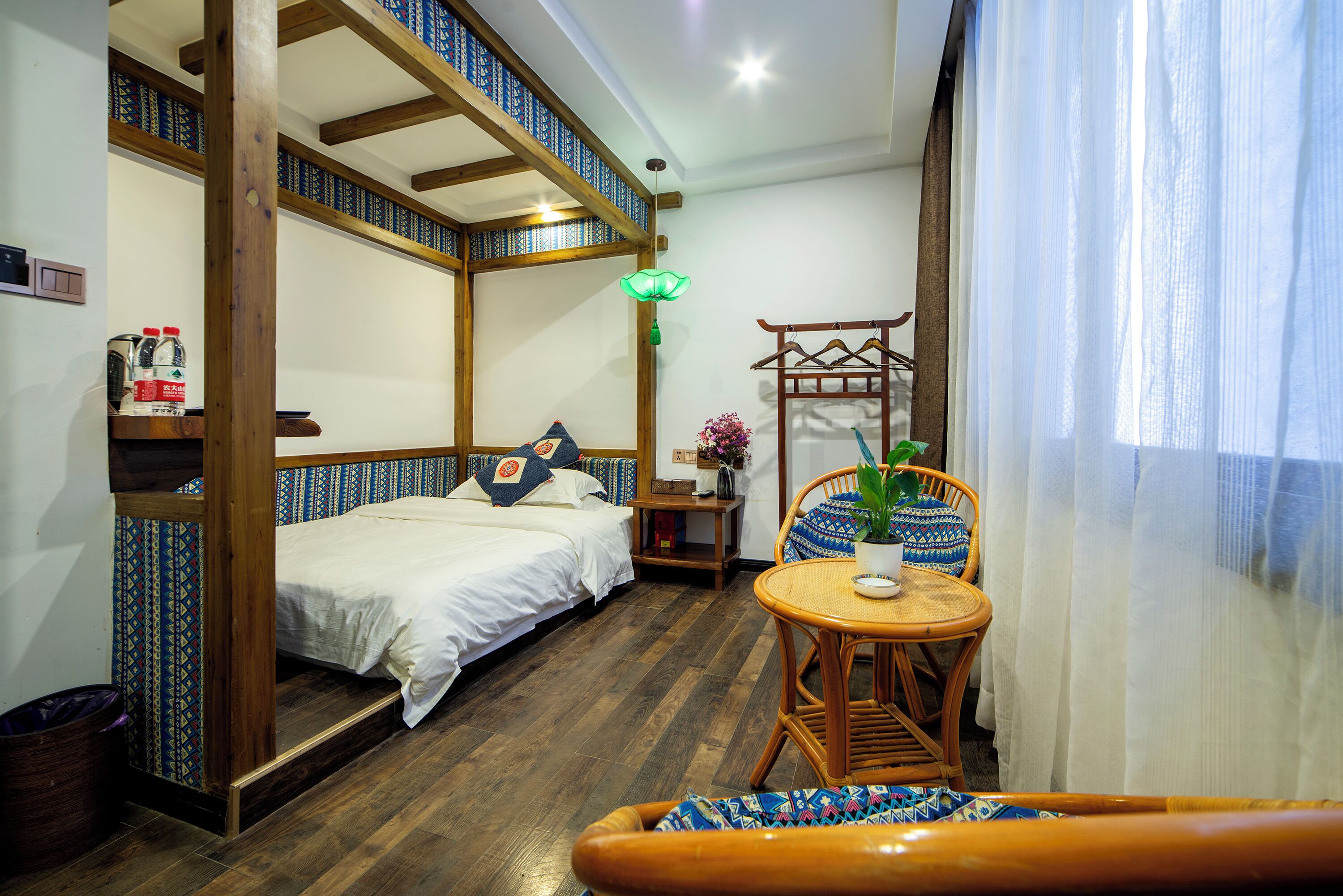 A room with a bed, a small table with a plant, and a chair.