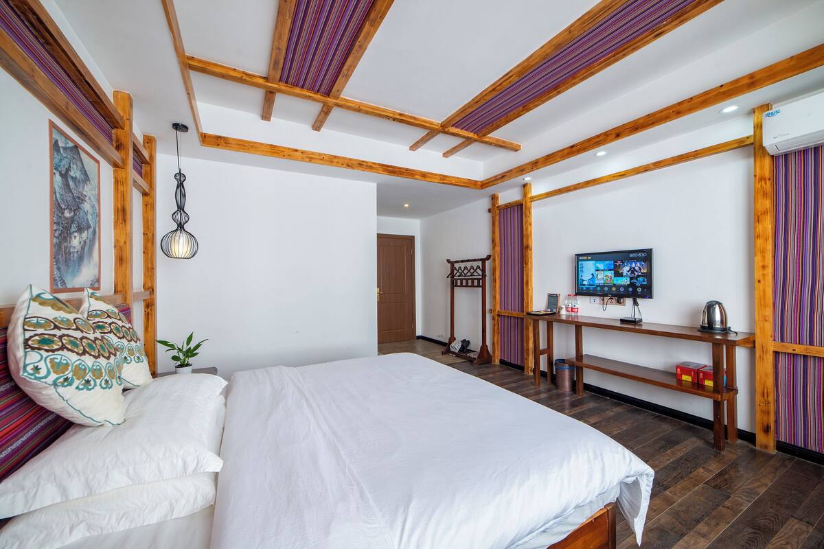 Ein Schlafzimmer mit einem großen Bett, Holzbalken, einem Fernseher und einem kleinen Tisch mit einem Wasserkocher.