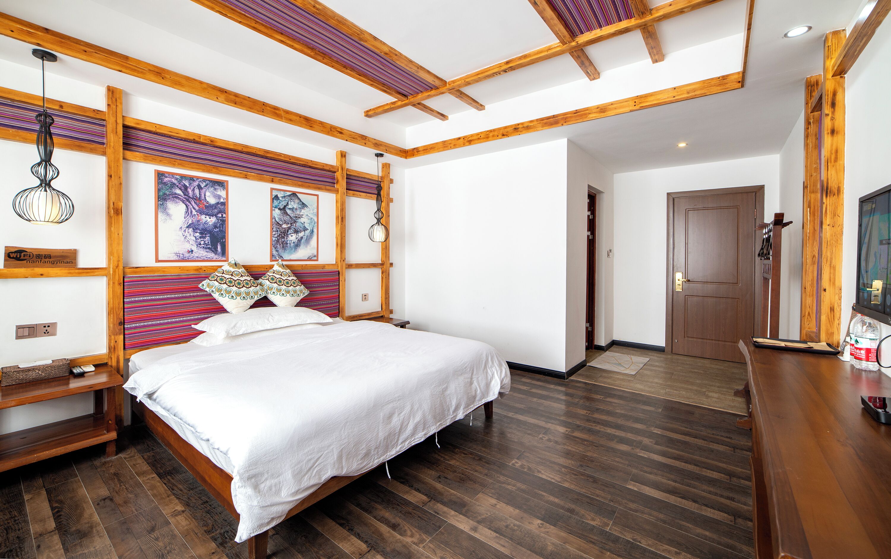 A bedroom with a wooden bed, a nightstand, a wall-mounted shelf, and a door with a coat rack.
