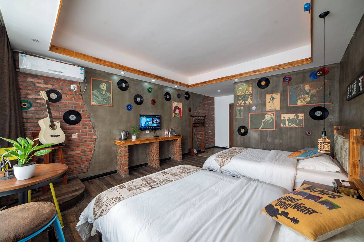 Ein Zimmer mit zwei Betten, einem Schreibtisch und einem Fernseher. Die Wände sind mit Schallplatten und Bildern dekoriert.
