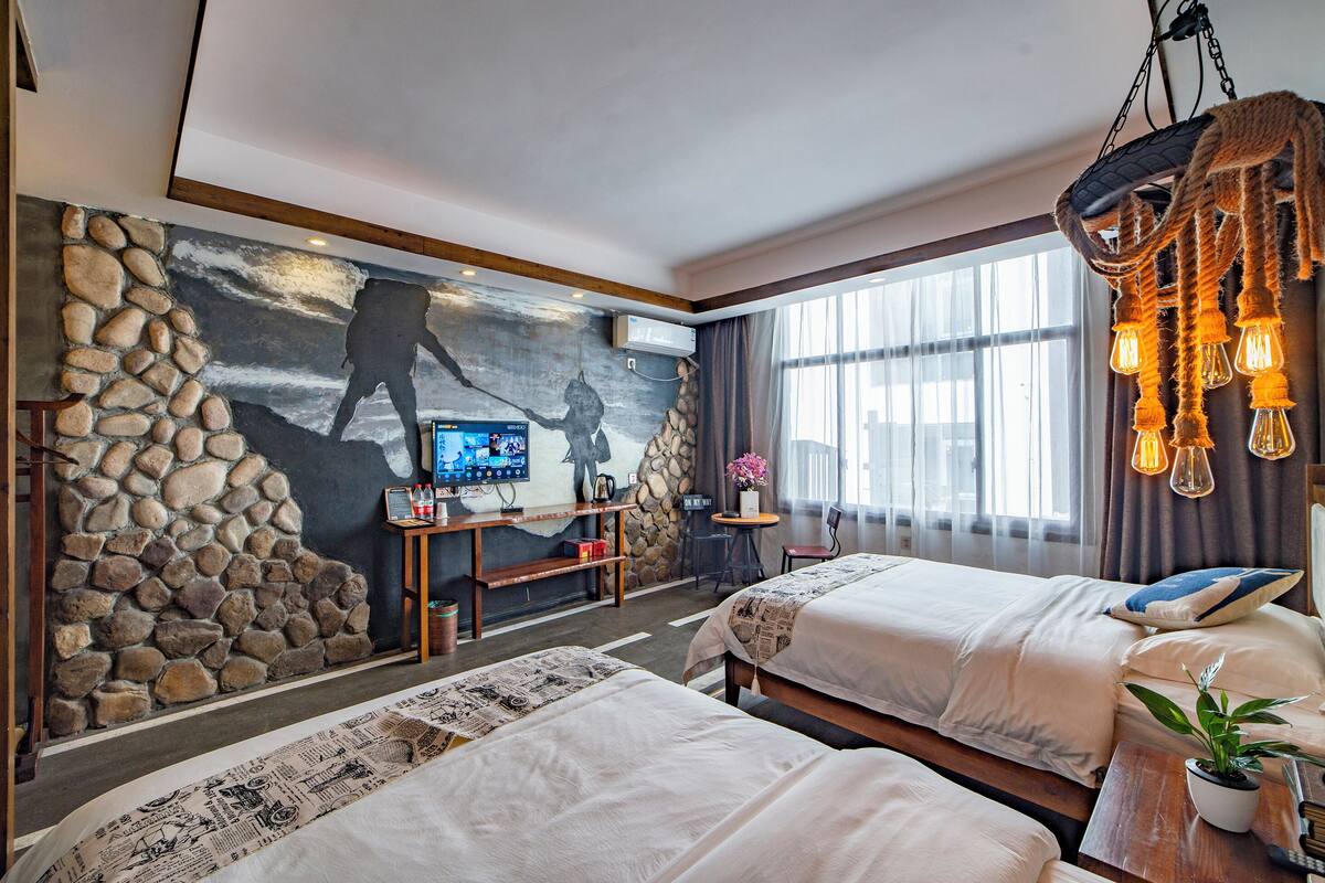 Ein Hotelzimmer mit zwei Betten, einer Steinwand, einem Wandfernseher und einem großen Fenster.