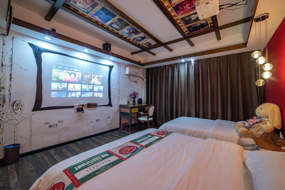 Ein Hotelzimmer mit zwei Betten, einem Schreibtisch, einem Stuhl und einem großen Bildschirm, der eine Diavorführung zeigt.