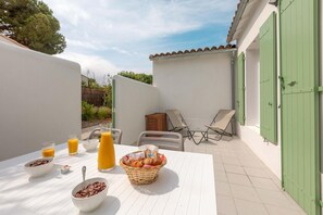 A patio with a table set for breakfast, including bowls of cereal and a basket of croissants, and a chair. - Apartment in Île de Ré with Terrace or Garden (RIVEDOUX PLAGE)