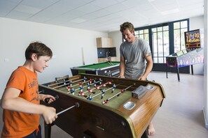 A room with a foosball table, a pool table, and a jukebox.