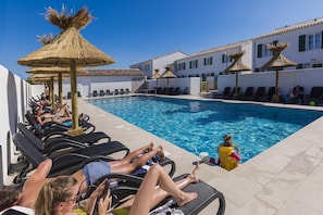 A poolside area with lounge chairs and umbrellas, a clear blue pool, and a building with white walls and green shutters in the background. - Apartment in Île de Ré with Terrace or Garden (RIVEDOUX PLAGE)