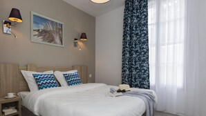 Ein Schlafzimmer mit einem Bett, zwei Wandlampen, einem gerahmten Bild und einem Fenster mit durchscheinenden Vorhängen.