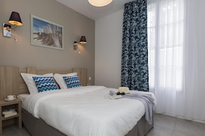 A bedroom with a bed, two wall-mounted lamps, a framed picture, and a window with sheer curtains. - Apartment in Île de Ré with Terrace or Garden (RIVEDOUX PLAGE)