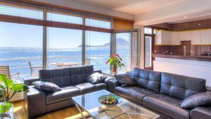 Een moderne woonkamer met een glazen salontafel, leren banken en uitzicht op zee door grote ramen.