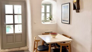 A dining area with a table, chairs, a door, a window, and a wall-mounted light fixture. - Traditional Village House 'Alba Lily' with heated plunge pool (Megalochori)