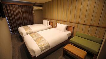 A hotel room with two beds, a green sofa, and a wooden bench.
