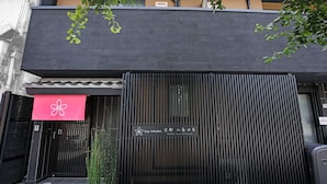 A building facade with a black gate, a red awning with a white flower, and a sign with Japanese characters.
