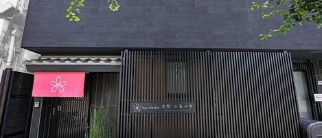 A building facade with a black gate, a red awning with a white flower, and a sign with Japanese characters.