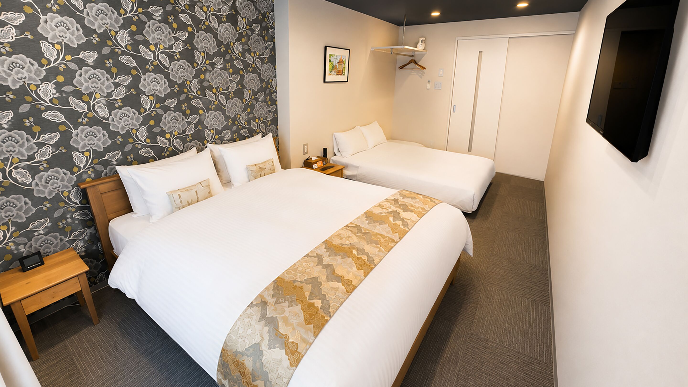A hotel room with a large bed, a smaller bed, a bedside table, a wardrobe, and a mirror.
