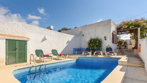 Ein Schwimmbecken mit Fliesenrand, umgeben von Liegestühlen und einer weißen Wand.