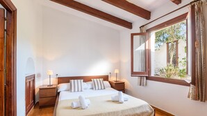 Ein Schlafzimmer mit einem großen Bett, zwei Nachttischen, einem Fenster mit Vorhängen und einem Holzbalken an der Decke.