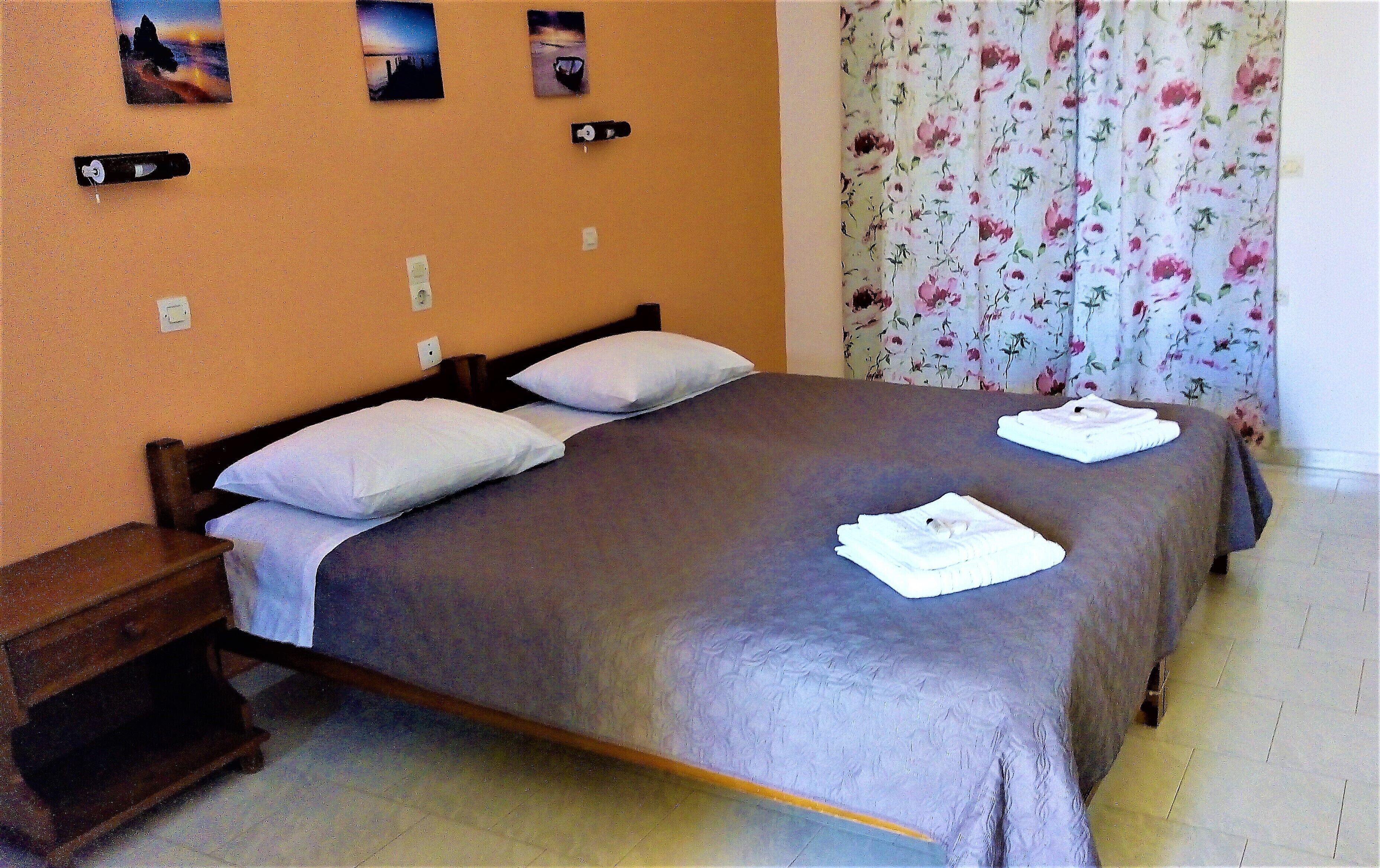 A neatly made bed with pillows, a wooden nightstand, and a floral curtain.