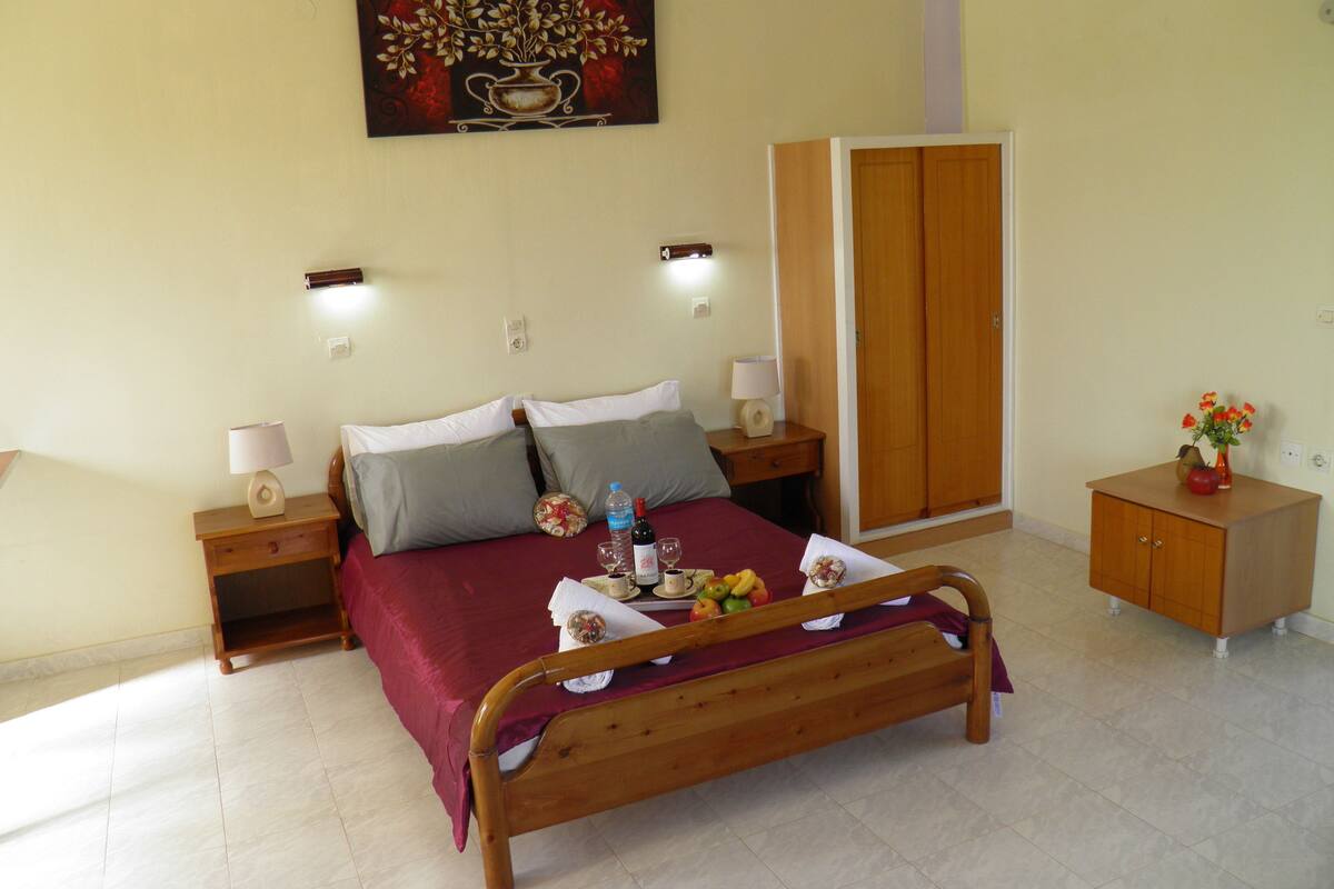 A neatly arranged bedroom with a wooden bed, two bedside tables with lamps, a wardrobe, and a small cabinet with a vase of flowers.