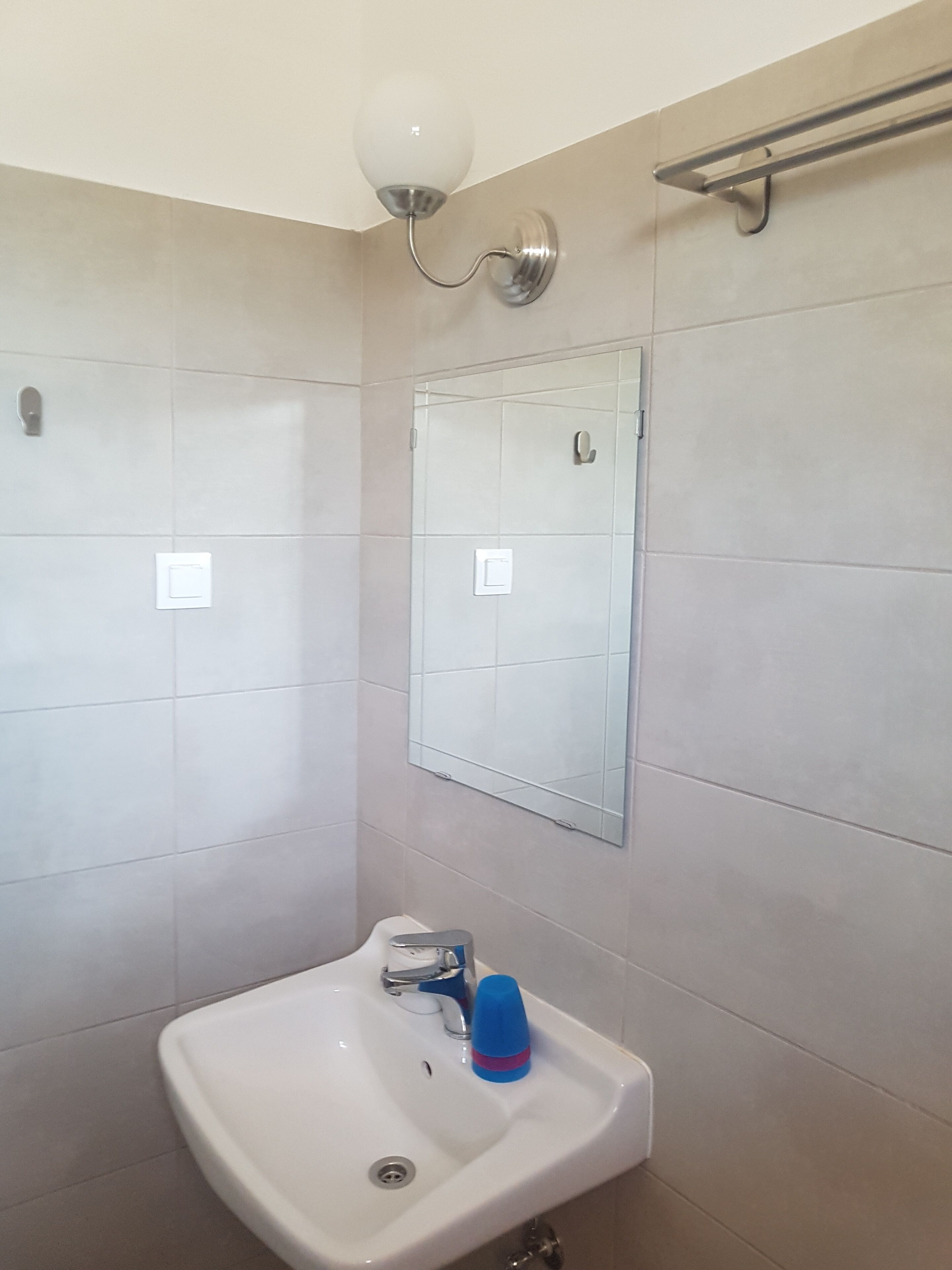 A bathroom with a white sink, a mirror, and a wall-mounted light fixture.
