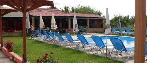 A poolside area with lounge chairs and umbrellas, a brick building in the background, and a clear sky.