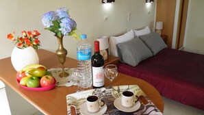 A hotel room with a bed, a bedside table with a vase of flowers, a bottle of water, a wine bottle, and a tray with cups and fruits. - Stars Hotel - Adults Only (Corfu)