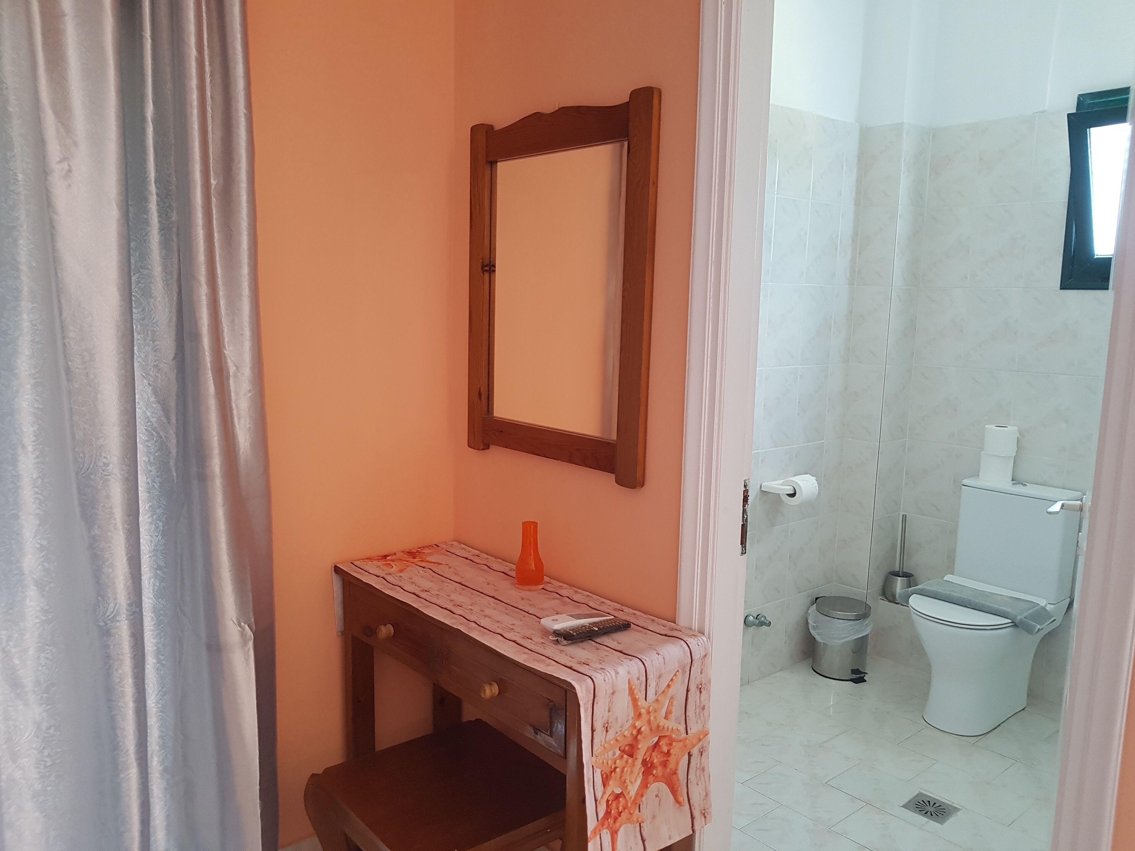 A bathroom with a wooden vanity, a mirror, a toilet, and a trash bin.