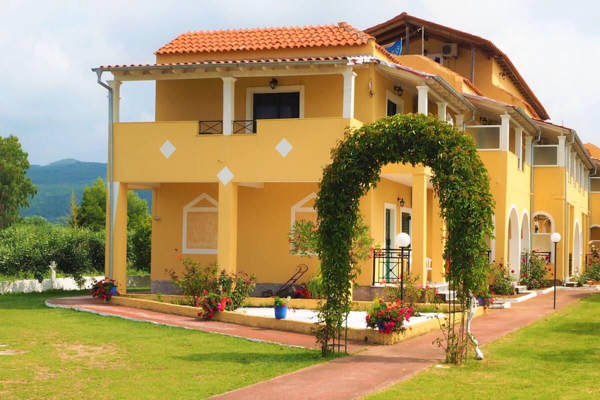A yellow building with a red-tiled roof, multiple balconies, and a central archway.