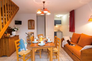 Ein gemütliches Wohnzimmer mit einer Holztreppe, einem Essbereich mit Tisch für vier Personen und einer Küche im Hintergrund.